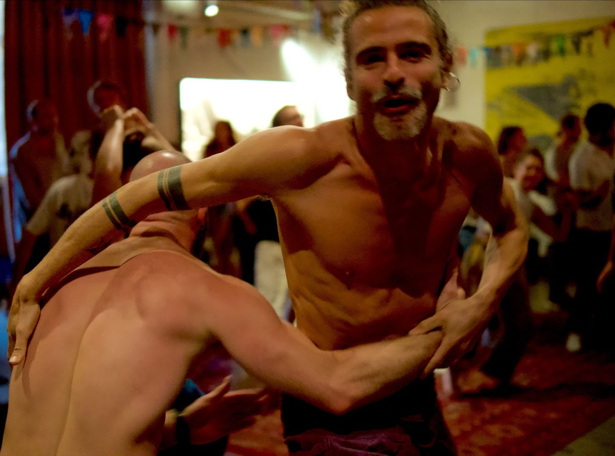 Two dancers embracing, one grinning at the camera